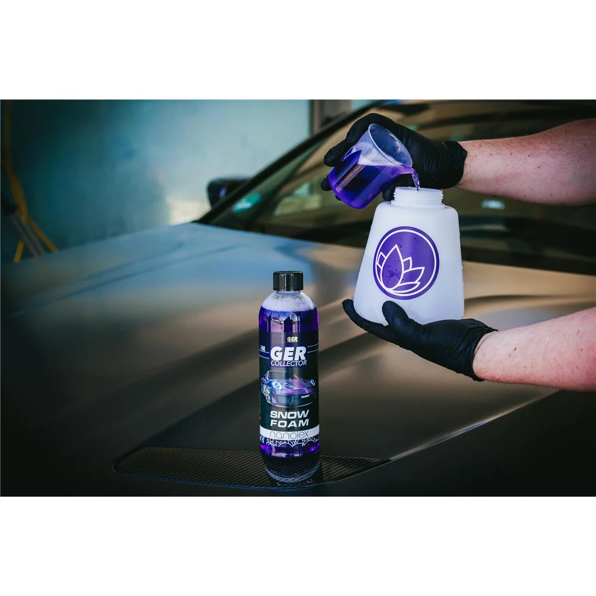 Eine Person mit schwarzen Handschuhen gießt eine violette Flüssigkeit aus einem Messbecher in eine weiße Flasche mit einem violetten Lotus-Logo. Eine große Flasche mit der Aufschrift „GERcollector SNOW FOAM“, die hochkonzentrierter Vorreiniger und hartnäckige Verschmutzungen entfernen soll, steht auf einer Motorhaube.